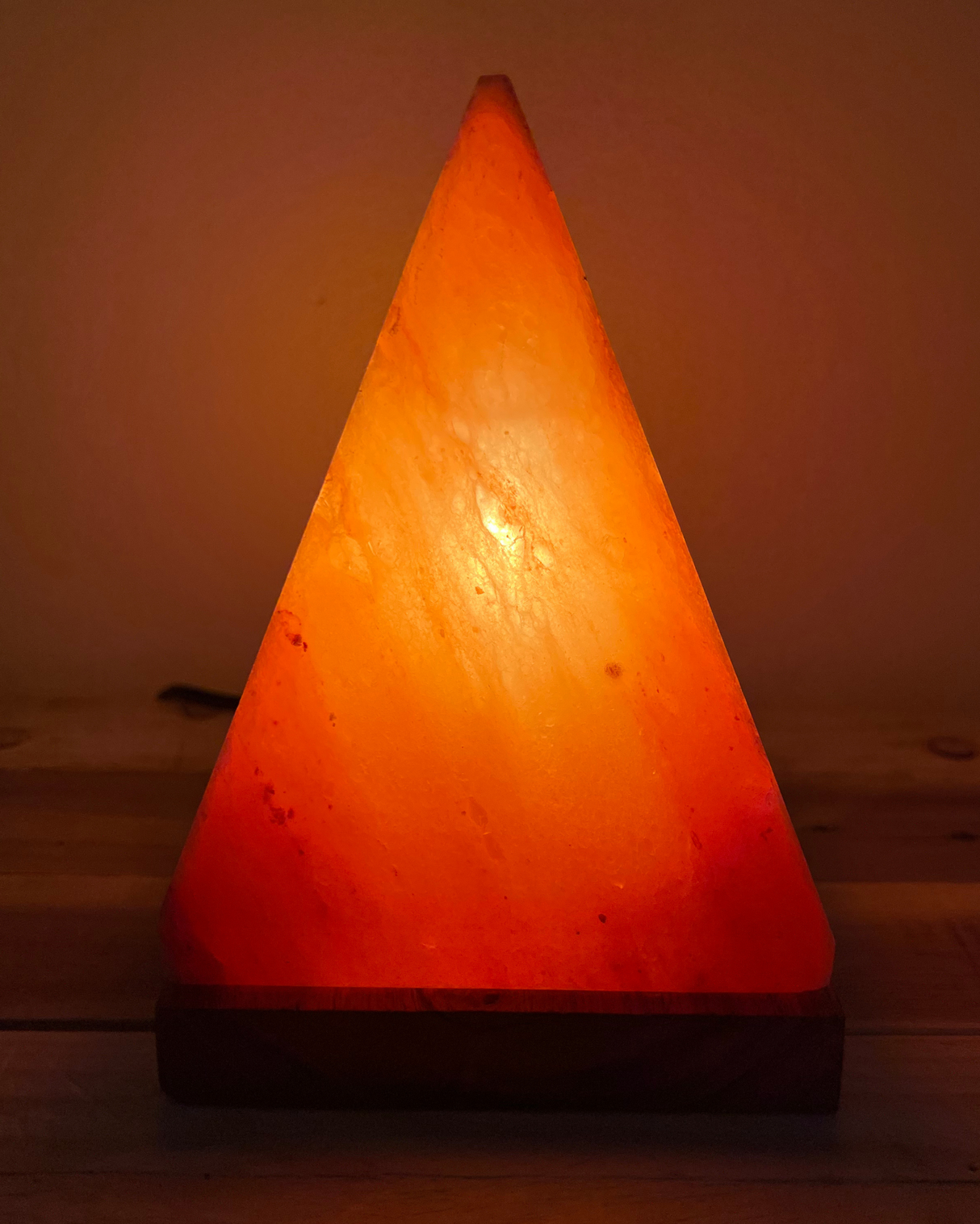Handgemaakte piramide zoutlamp op houten voet, zuivert lucht en straalt warm, rustgevend licht voor een sfeervol interieur