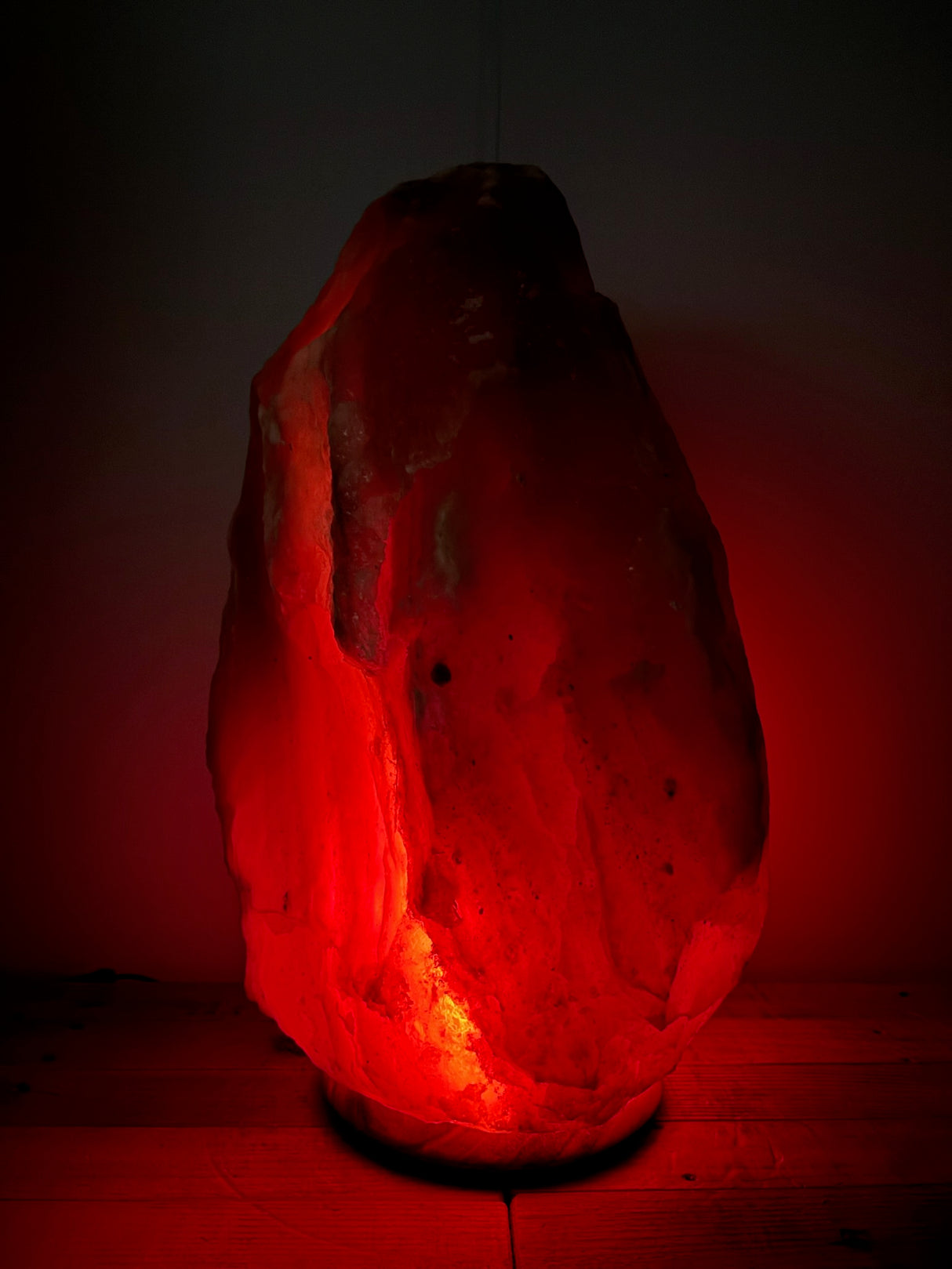 Donkere Himalaya zoutlamp 40–45 kg met warme roodbruine gloed op robuuste houten voet