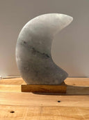 maanvormige Himalaya zoutlamp in roze, grijs en wit met zachte gloed en houten voet