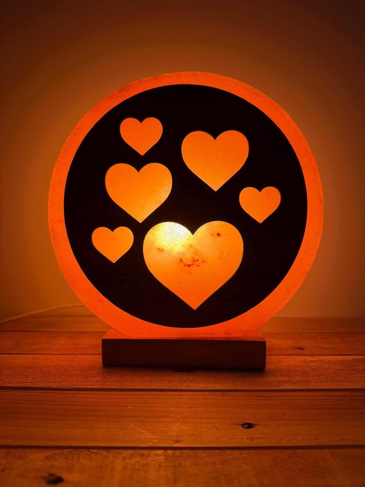 Handgemaakte Himalaya zoutlamp in 3D hartvorm met warme gloed en houten voet.