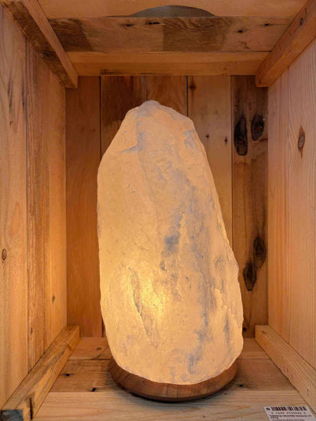 Witte Himalaya zoutlamp 6-8 kg aan, warm gloeiend op houten voet in houten kist