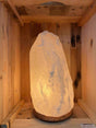 Witte Himalaya zoutlamp 6-8 kg aan, warm gloeiend op houten voet in houten kist