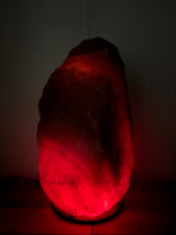 Donkere Himalaya zoutlamp 70–80 kg met diepe rood/oranje gloed op houten voet